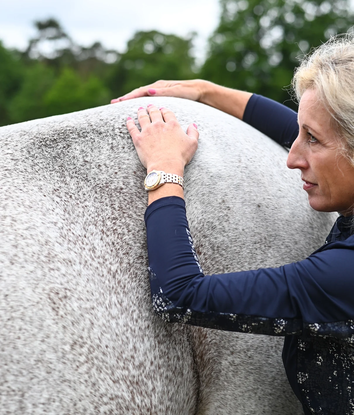 Sabrina Barmentloo, osteopaat bij 'Osteopaat voor je Paard', voert een zorgvuldig onderzoek uit op de rug van een wit paard. Haar aandachtige blik en zachte aanraking illustreren haar deskundigheid, ondersteund door uitgebreide opleidingen in onder andere paardenosteopathie, sportmassage en cranio sacraal technieken.