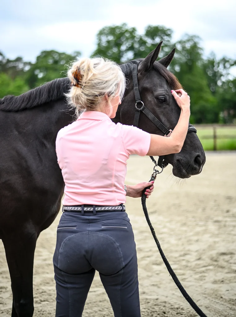 Sabrina Barmentloo van 'Osteopaat voor je Paard' inspecteert het hoofd van een zwart paard tijdens een consult. Deze afbeelding illustreert een pagina over voedingsadvies voor paarden, gericht op het bevorderen van een gezond en gelukkig paard door middel van optimale voeding.